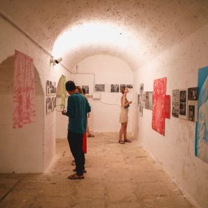 visitatori che guardano i quadri della mostra sul tarantismo nella sala della tabaccaia